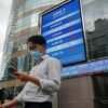 People walk past a screen displaying the Hang Seng stock index outside Hong Kong