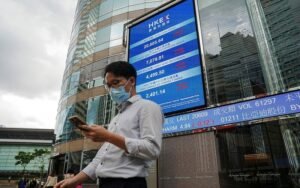 People walk past a screen displaying the Hang Seng stock index outside Hong Kong