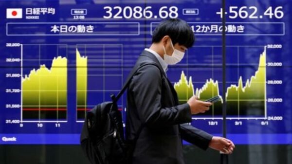 A man walks past an electric monitor displaying Japan's Nikkei share average and recent movements