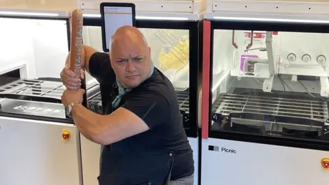 Lee Kindell Taking the stance of a baseball batter, Lee Kindell holds a roll of pizza dough as if it's a bat and makes a mock-serious game face. 