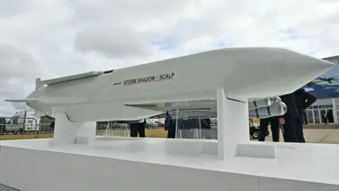 AFP via Getty Images A long white missile on a stand with people stood around it. It has the words storm shadow/scalp on it and has wings at the back and a pointy nose