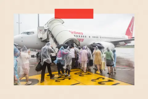 VCG via Getty Images A group of people in clear waterproof ponchos boarding a plane